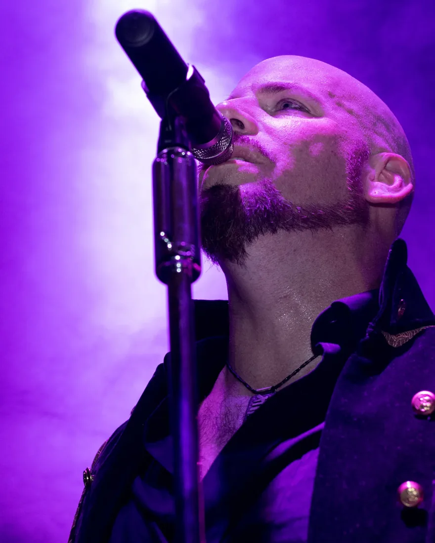 A vocalist mid-note at the microphone under violet stage light